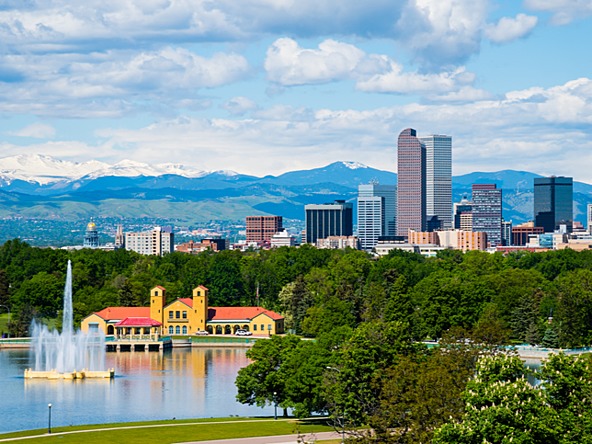 Denver Colorado view, tall buildings and a city park in the foreground with mountains in the background